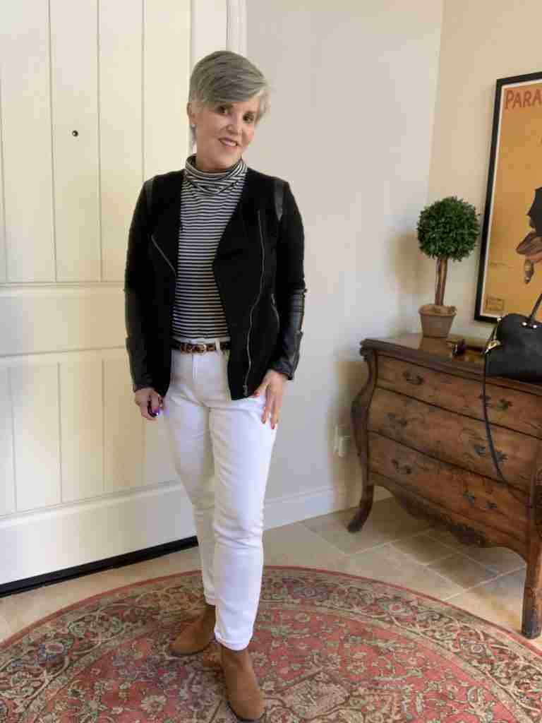 A black moto jacket with a black and white turtleneck, white jeans, and a skinny leopard belt.  Black leather doctor's bag and brown suede booties complete the white jeans in winter look