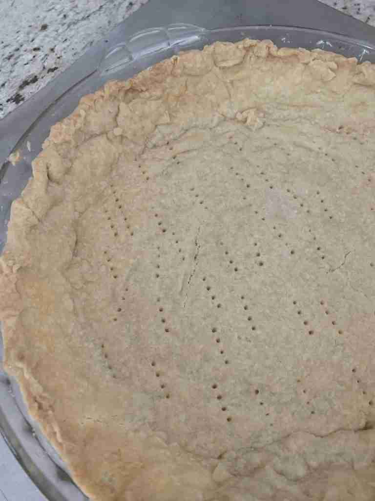 a photo of a raw pie crust in a glass pie plate as part of the steps of how to make a home-made pie crust.