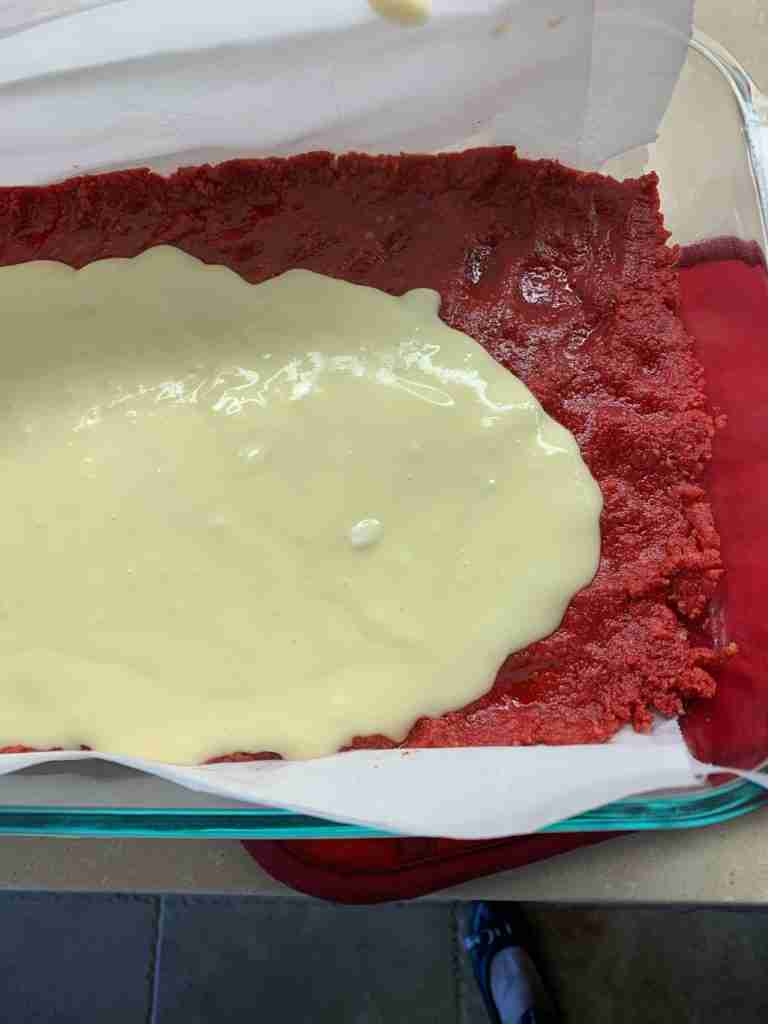 Pouring the creamy filling over the red base dough.