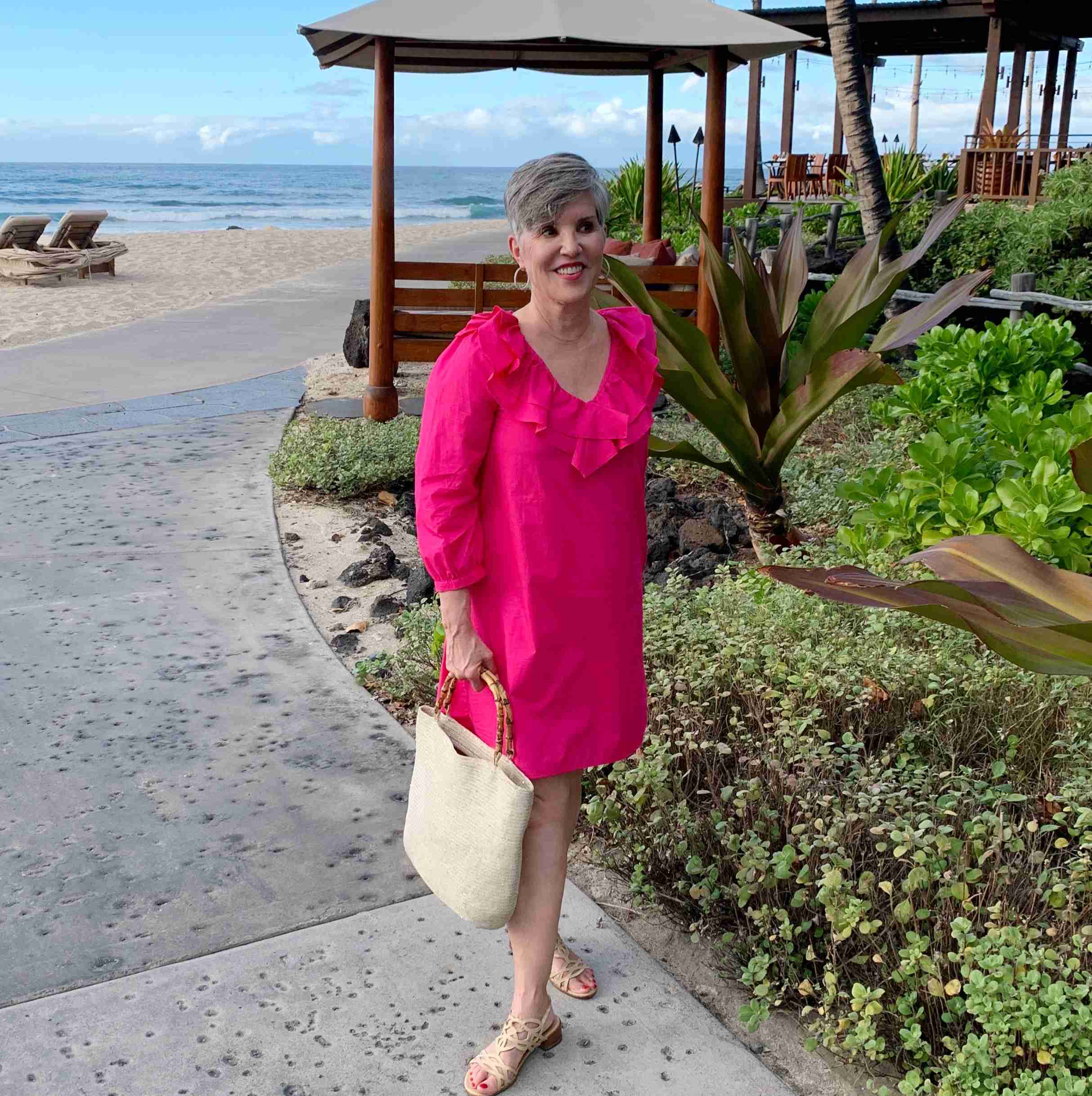 me in a bright pink ruffled neck cotton dress standing in front of the beach at the Four Seasons hotel on the Big Island of Hawaii!