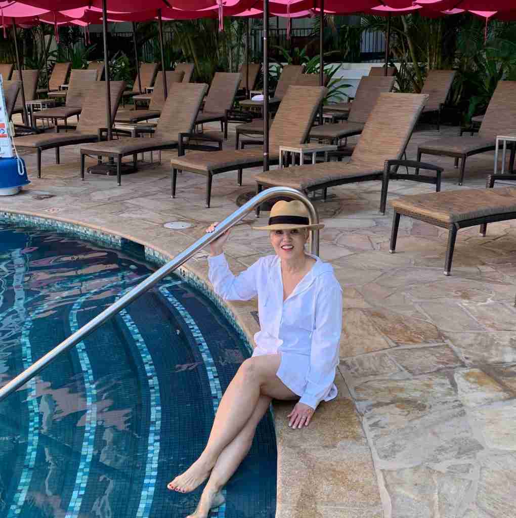 Sitting by the pool in a hat and white hooded cover-up.