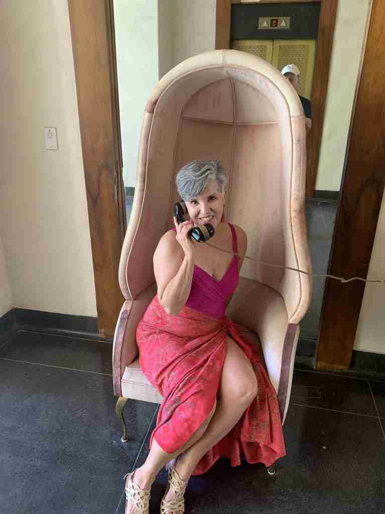 Me pretending to make a call on an old-fashioned phone while sitting in a high-backed chair wearing a fuchsia tank and Polynesian sarong.