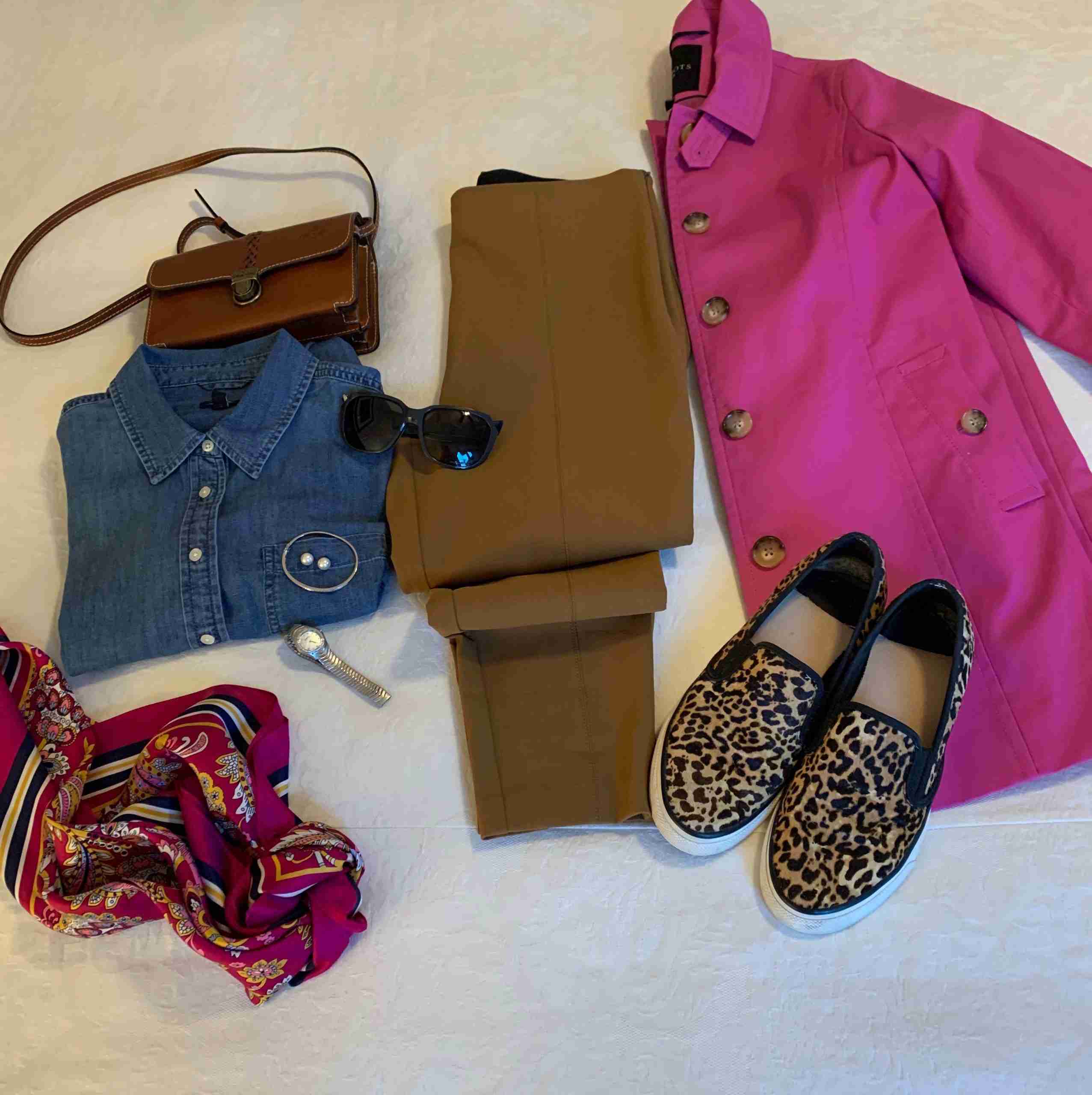 pink/violet coat with tobacco brown slim pants, a brown crossbody bag, a denim shirt, and a vibrant pink, paisley scarf.