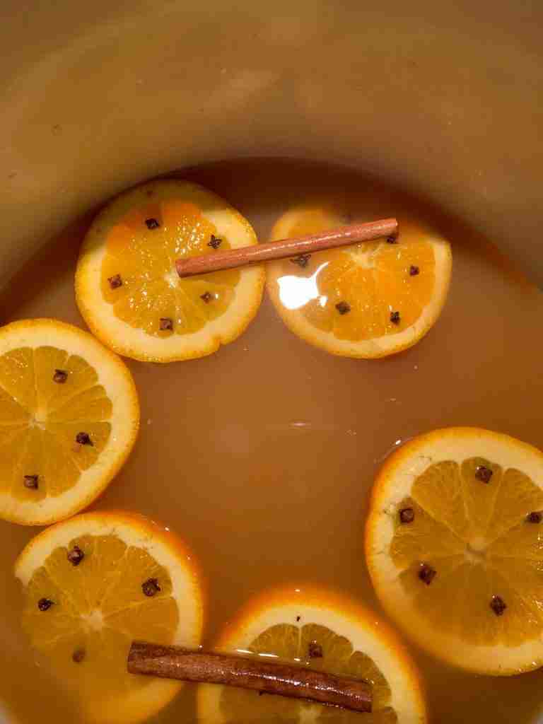 A pot of the best cider with several orange slices floating in it.  The slices have been studded with cloves.