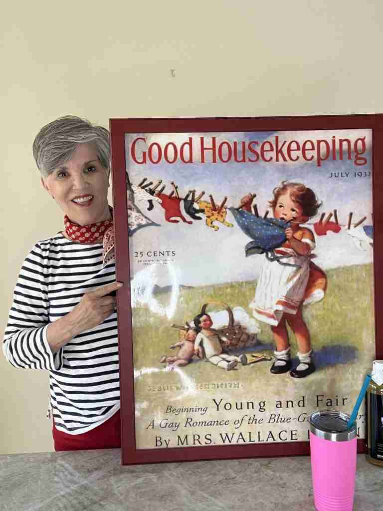 I am wearing a navy striped tee, with a red bandana and pretty zirconium earrings. I am holding a darling Good Housekeeping print of a little girl pinning up clothing on a clothesline.