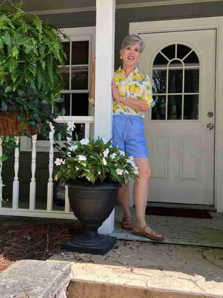 This is one example of the many late summer outfits. 
Isn't this a darling look with the lemon print cotton long-sleeved shirt, the linen shorts, the nude sandals, and the lemon earrings?   I am at my brother's home on his coach house porch which is adorned with loads of summer flowers.  