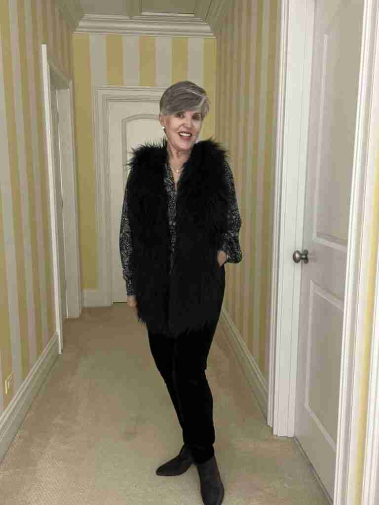 In this second casual date night outfit, I am wearing a black print blouse under a faux fur vest with black velvet jeans and grey booties.  The blouse has multiple colors in the vest including cream, mustard, burgundy and blue.