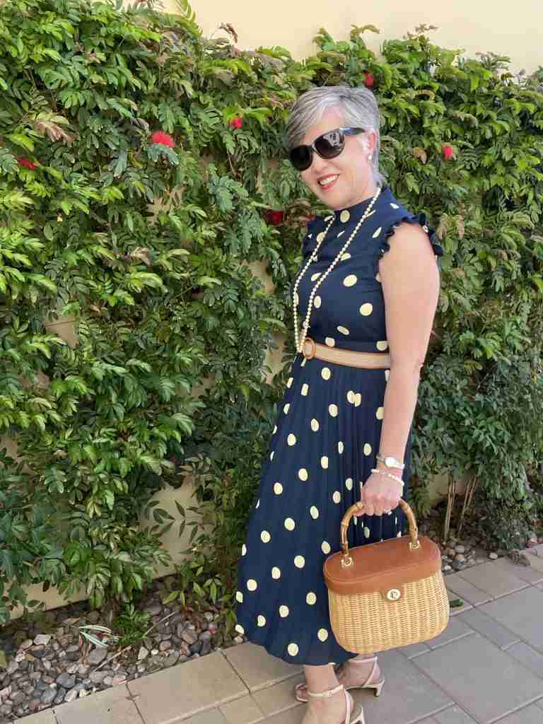 Here is the navy polka dot dress worn with pearls and a wicker handbag. I have on cream stappy sandals with a razor heel as well as a khaki canvas belt with honey-colored leather trim.