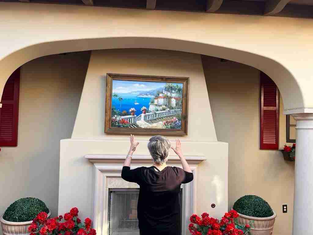 Here's the painting mounted on the chimney as a focal point.  You can see the green topiary balls and a bit of the geraniums in pots adjacent to the fireplace on the concrete patio.