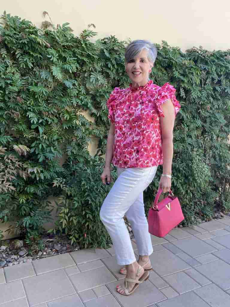 Here I am wearing white denim straight-leg jeans with the same ruffled top and pink bag, but now I am wearing tan flat sandals.  This i a side view of the look.  I am standing in front of a wall of green vines in my California front yard.