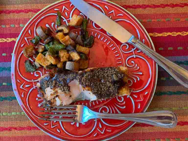 A red plate with a gorgeous piece of spicy salmon bake. And there is a batch of roasted sweet potatoes and green peppers on the side.