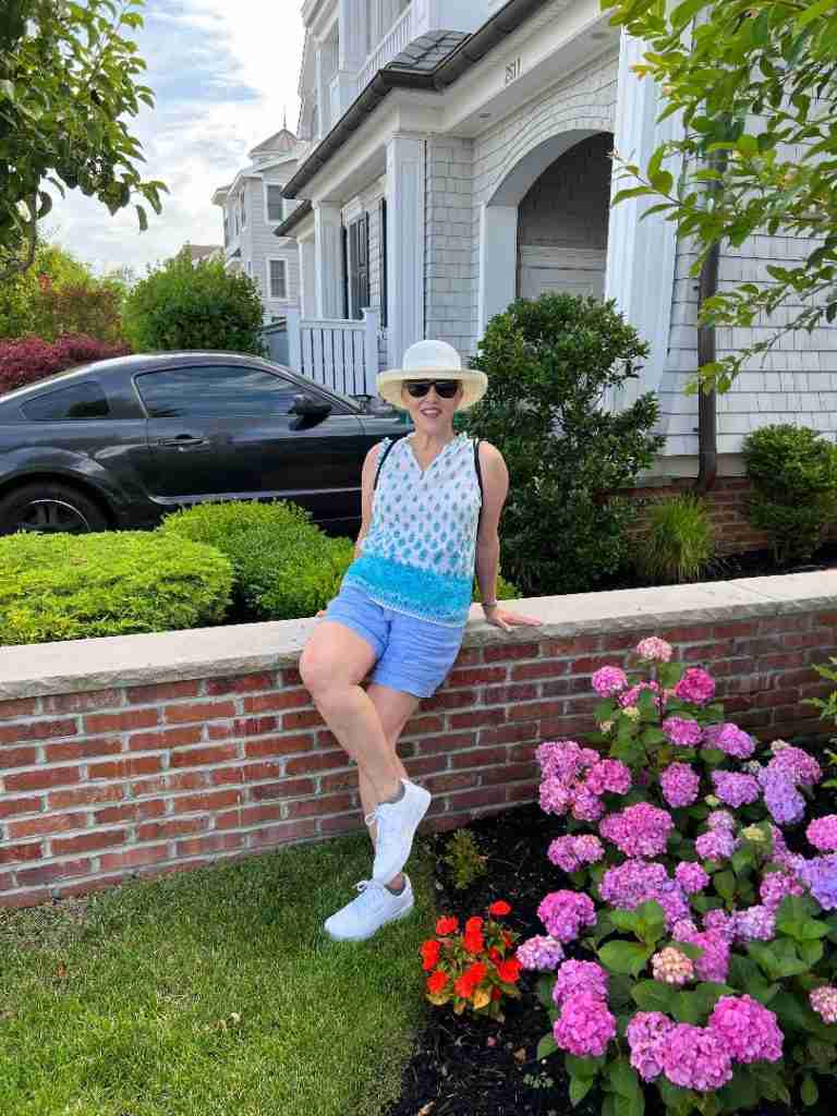 Here I a  wearing a sleeveless foulard cotton tank in blue tones with blue linen shorts and white sneakers.  My hat is broad-brimmed and my sunglasses are ovrtsized.