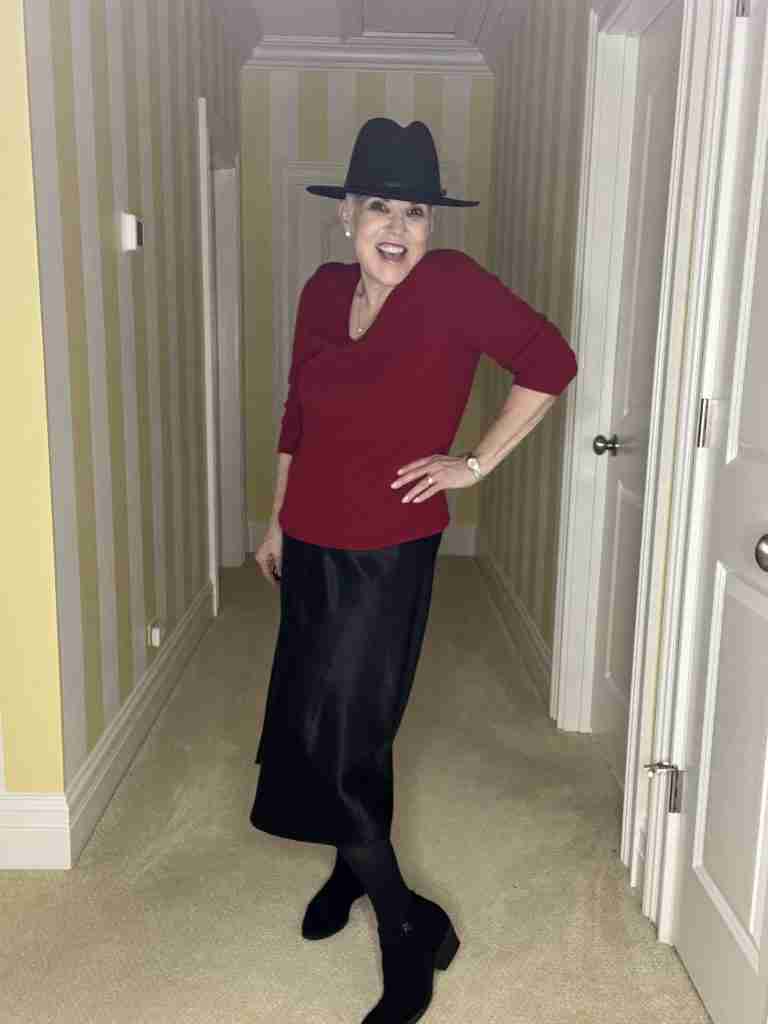 I am wearing a red V-neck cashmere sweater over the black slip dress which make it look like a satin skirt.  I added a black hat as well as black suede booties, and black tights.