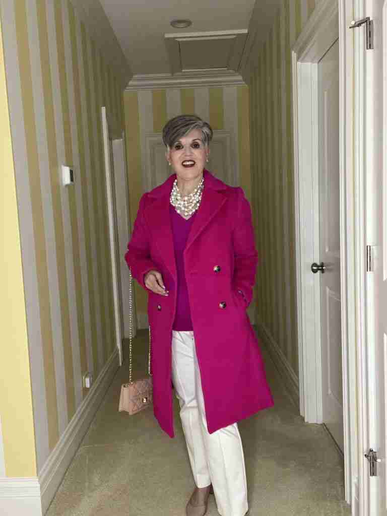 A classic coat that's fuchsia is worn over a fuchsia v-neck cashmere sweater and a multi-stranded pearl choker.  My pants are winter white dress pants and my bag and shoes are nude