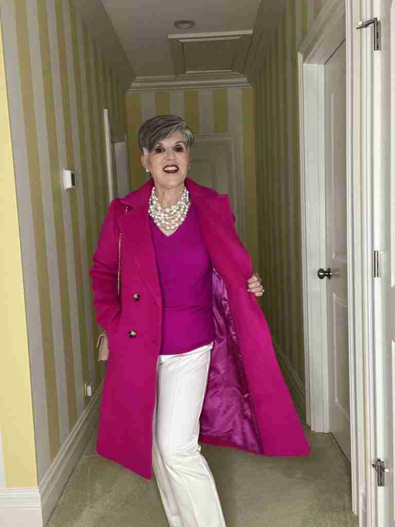 A classic coat that's fuchsia is worn over a fuchsia v-neck cashmere sweater and a multi-stranded pearl choker.  My pants are winter white dress pants and my bag and shoes are nude.